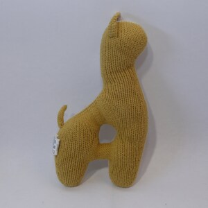 May include: A knitted yellow stuffed animal shaped like a giraffe. The giraffe has a white patch on its head.