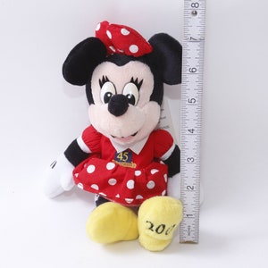 May include: Red and white polka dot dress with a red bow and a white bow on top of the head. The dress has a white patch with the text "45th Anniversary" and the number "2001" on the bottom of the dress.  The plush toy is approximately 7 inches tall.