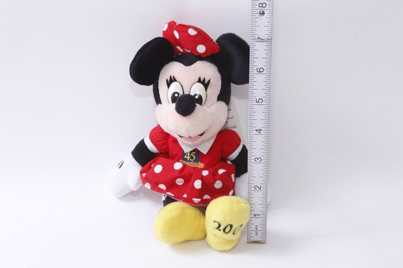 May include: Red and white polka dot dress with a red bow and a white bow on top of the head. The dress has a white patch with the text "45th Anniversary" and the number "2001" on the bottom of the dress.  The plush toy is approximately 7 inches tall.