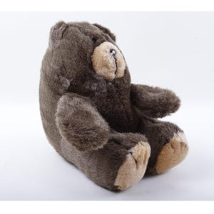 May include: A plush teddy bear with dark brown fur and a lighter tan muzzle. The stuffed animal is seated in a profile position, featuring a small black nose, rounded ears, and tan-colored paw pads on its feet. The texture of the fur is soft.