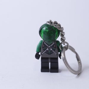 Op de afbeelding: Een groene en zwarte Lego minifiguur sleutelhanger met een groene helm en een zilveren ketting.