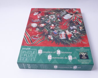 May include: A green box with a red and green Christmas wreath on the front. The box is for a 500 piece jigsaw puzzle titled "Memories of Christmas" and "Souvenirs de Noel". The box also features a small image of a silver angel ornament.