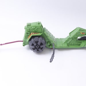 May include: Green plastic toy vehicle with a snake head design. The vehicle has a large wheel on the back and a smaller wheel on the front. The vehicle has a purple rope attached to the front.