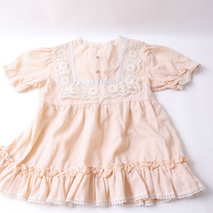 May include: A pale pink baby dress with a lace trim and a ruffled hem.