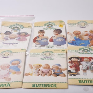Könnte beinhalten: Eine Sammlung von Vintage-Butterick-Schnittmustern für Cabbage Patch Kids-Kleidung und -Zubehör. Die Muster zeigen Illustrationen der Puppen in verschiedenen Outfits, mit dem Butterick-Logo unten.