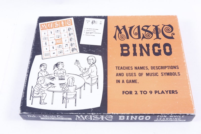 May include: A vintage game box for "Music Bingo" with a colorful illustration of children playing the game. The box features the text "Music Bingo" in a stylized font and the tagline "Teaches names, descriptions and uses of music symbols in a game." The box is orange and black with a white illustration.