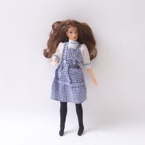 May include: A doll with brown hair wearing a blue and white gingham dress and black tights.