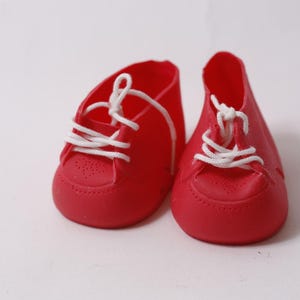 May include: A pair of bright red baby shoes with white laces. The shoes have a classic sneaker design with a rounded toe and small perforations. The laces are tied in a simple knot.