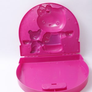 May include: Pink plastic Hello Kitty lunchbox with a molded image of Hello Kitty and a bear. The lunchbox is open and the inside is empty.
