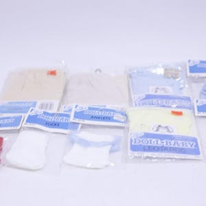 May include: A collection of packaged baby doll clothing items, including socks, anklets, and leotards. The items are in various colors such as red, white, blue, and yellow. Each item is sealed in a clear plastic bag with a blue and white label.