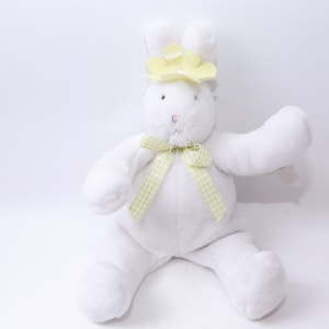 May include: A white plush bunny rabbit wearing a yellow flower headband and a green and white checkered bow.
