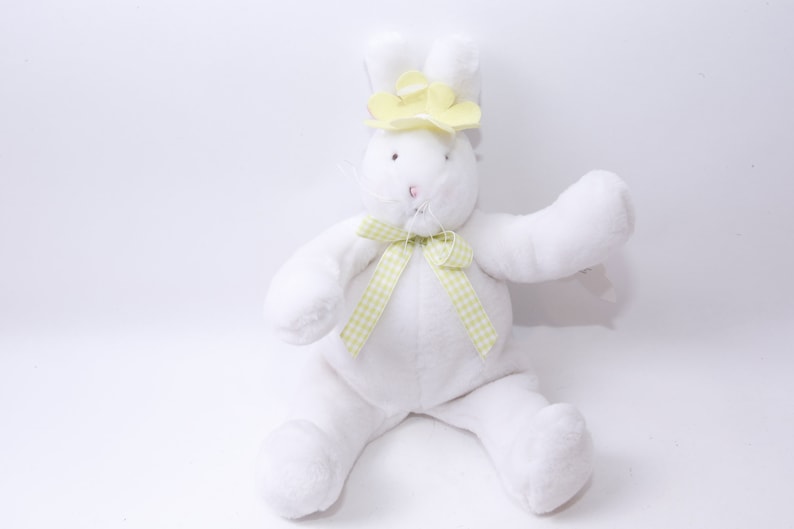 May include: A white plush bunny rabbit wearing a yellow flower headband and a green and white checkered bow.