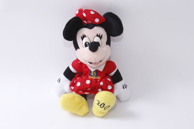 May include: A red and white polka dot dress with a red bow on the head, a plush Mickey Mouse doll wearing a red and white polka dot dress with a red bow on the head, and the text "45 Disneyland 2000" on the dress.