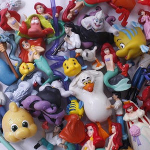May include: A collection of colorful plastic figurines of characters from the Disney movie The Little Mermaid. The figurines include Ariel, Ursula, Flounder, Sebastian, and others.