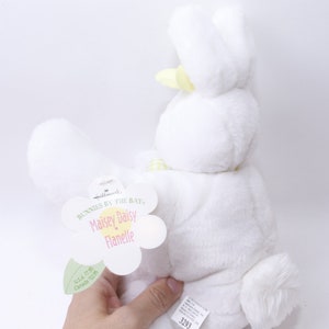May include: White plush bunny with yellow ears and a yellow bow. The bunny is holding a tag that says "Bunnies by the Bay, Maisie Daisy Flanelle".
