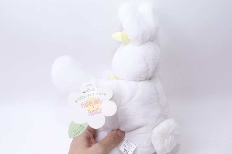 May include: White plush bunny with yellow ears and a yellow bow. The bunny is holding a tag that says "Bunnies by the Bay, Maisie Daisy Flanelle".