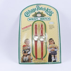 May include: A package containing two red Cabbage Patch Kids wrist watches with adjustable bands. The package features a Cabbage Patch Kid doll on each side.