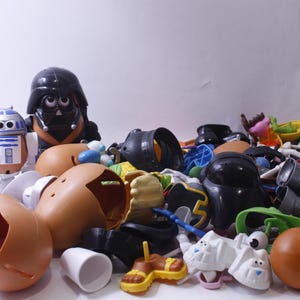 May include: A collection of plastic toy parts, including a Darth Vader head, an R2-D2 head, and various potato head pieces. The parts are in various colours, including brown, black, white, and blue.