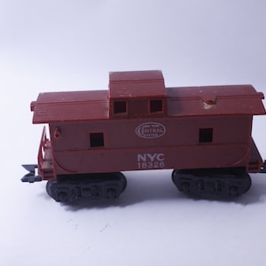 May include: A red toy train caboose with black wheels and the text "NYC 18326" and "New York Central System" printed on the side.
