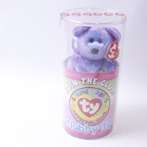 May include: A purple and blue Beanie Baby named "Clubby Ivy" in a clear plastic tube. The tube has a pink and white label that says "Join the Club! Beanie Babies Official Club".