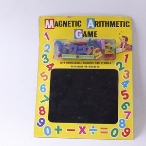 Puede incluir: Un juego de aritmética magnético amarillo y negro con una pizarra y números y símbolos magnéticos de colores. El juego incluye los números del 0 al 9, más, menos, multiplicar, dividir e igual.