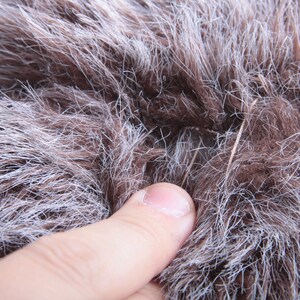 May include: Close-up of a brown and white faux fur fabric with a small hole in the center. A finger is touching the fabric.