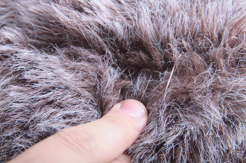 May include: Close-up of a brown and white faux fur fabric with a small hole in the center. A finger is touching the fabric.