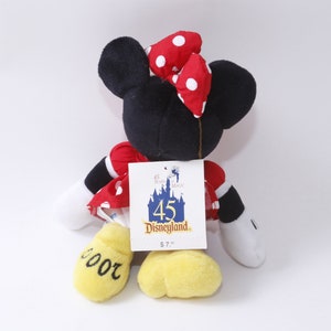 May include: A red and white polka dot plush Minnie Mouse toy wearing a red bow with white polka dots. The toy is holding a tag that says "45 Disneyland $7.99". The toy's feet are yellow and have the number "2000" written on them.