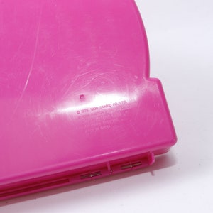 May include: A pink plastic case with the text "&copy; 1976, 1999 SANRIO CO., LTD. ALL RIGHTS RESERVED. MADE IN CHINA" printed on the bottom.