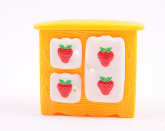 May include: A yellow toy cabinet with four white doors, each decorated with a red strawberry. The cabinet has a wood-grain texture.