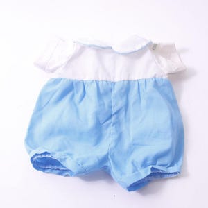 May include: A baby romper in a light blue and white color scheme. The top is white with a rounded collar and short sleeves. The bottom is light blue with a gathered waist and short legs.