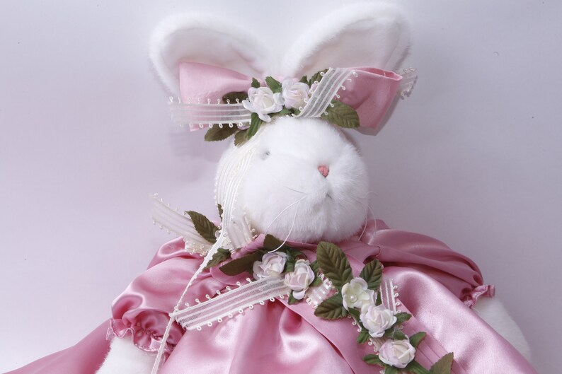 Peut inclure: Un lapin en peluche blanc portant une robe en satin rose avec une bordure en dentelle blanche et un n&oelig;ud rose avec de la dentelle blanche et des accents floraux.