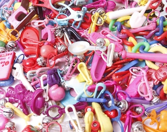 May include: A large collection of colorful plastic keychains featuring various shapes and designs, including a calculator, a wrench, a frying pan, a baseball bat, a cow, and a bell.