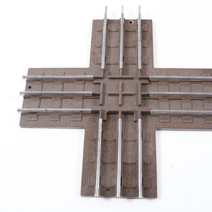 May include: A brown plastic model train track crossing with four sets of tracks, each with three rails.