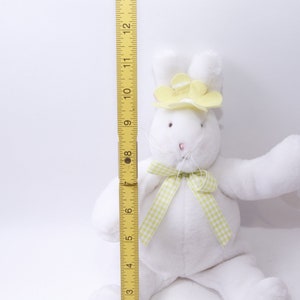May include: White plush bunny rabbit wearing a yellow flower hat and a green and white gingham bow. The bunny is approximately 10 inches tall.