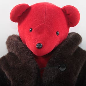 May include: A red teddy bear wearing a brown fur coat. The bear has black eyes and a black nose.