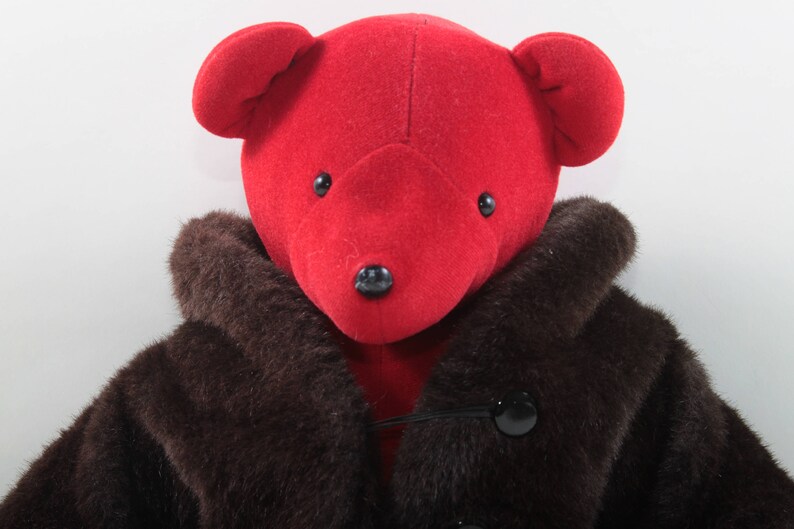 May include: A red teddy bear wearing a brown fur coat. The bear has black eyes and a black nose.