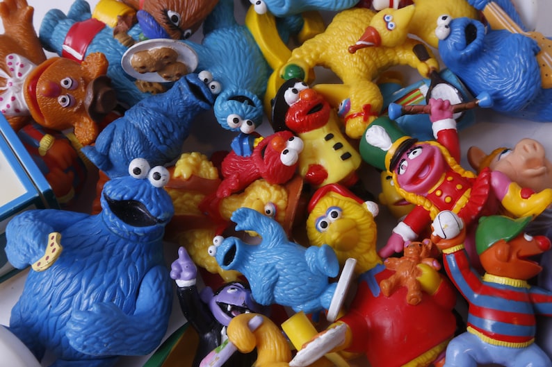 May include: A collection of Sesame Street character figurines, including Cookie Monster, Elmo, Big Bird, and Bert and Ernie. The figurines are made of plastic and are brightly colored.