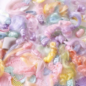 May include: A collection of pastel-colored doll hair, combs, and accessories. The assortment includes shades of pink, purple, yellow, and blue. Various hair pieces are curled, straight, and styled with bows and barrettes. The image is a close-up shot.