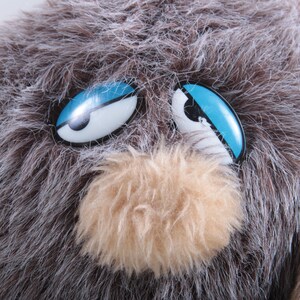May include: A brown and gray furry toy with blue eyes. The toy has a brown fuzzy nose and a white mouth.