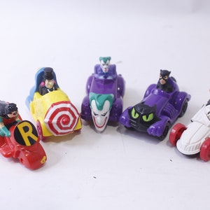 May include: A set of six Batman themed toy cars featuring Robin, The Joker, Catwoman, and The Penguin. The cars are made of plastic and are brightly colored.