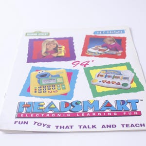 May include: A colourful brochure advertising Headsmart electronic learning toys for children. The brochure features images of Sesame Street characters and children playing with the toys. The text on the brochure reads "Headsmart Electronic Learning Fun" and "Fun Toys That Talk and Teach".