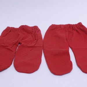 May include: Two pairs of red baby pants are laid out on a white surface. The pants have an elastic waistband and are made of a soft, possibly knit, material. The pants are designed for infants.