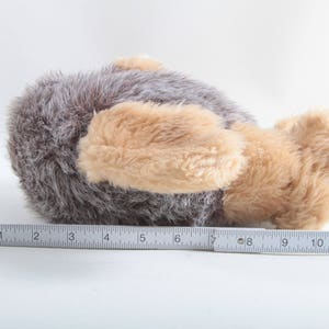 May include: A plush toy in the shape of a brown and tan dog lying on its side. The dog has a long, fluffy tail and a soft, cuddly texture.