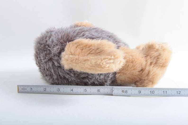 May include: A plush toy in the shape of a brown and tan dog lying on its side. The dog has a long, fluffy tail and a soft, cuddly texture.