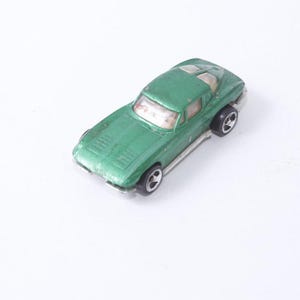 May include: A green die-cast toy car with silver accents. The classic car has a sleek design with visible hood vents and black wheels. The toy car is a miniature replica of a vintage sports car.