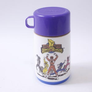 May include: A purple and white thermos with a picture of the Mighty Morphin Power Rangers. The text "Mighty Morphin Power Rangers" is printed on the thermos.