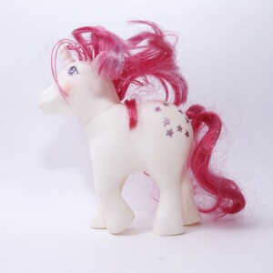 May include: A white pony toy with pink hair and a silver star design on its side.