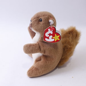 May include: A brown plush squirrel toy with a fluffy tail and white belly. The stuffed animal has a red heart-shaped tag with the words "Beanie Baby" and a yellow star.