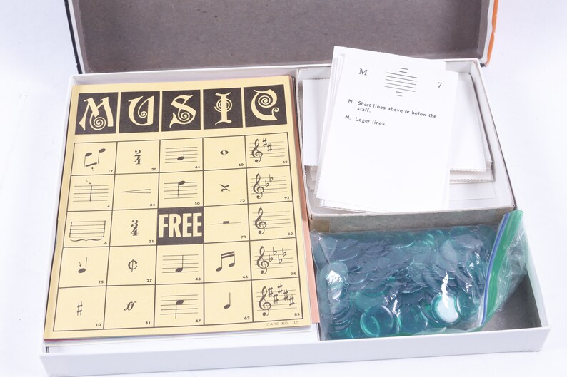 May include: A vintage board game called "MUSIC" with a yellow game board, a set of instructions, and a bag of green game pieces. The game board has a grid with musical notes and symbols.